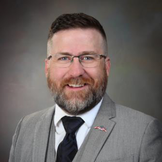 Photo of  Nathan E. Miller, smiling with beard, grey suit, and glasses